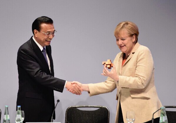 Chinese Premier Li Keqiang (L) presents a burr puzzle to German Chancellor Angela Merkel as they attend a China-Germany economic and technological cooperation forum in Berlin, Germany, Oct. 10, 2014. (Xinhua/Li Xueren)