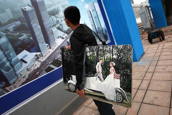 A man carrying his wedding photo stops to check out a property promotion in Changsha, Hunan province. New home prices in November dropped 1.57 percent year-on-year in 100 cities monitored by the China Index Academy. ZHOU QIANG/CHINA DAILY