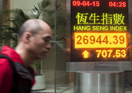 A man walks near an electronic board showing the Hong Kong share index outside a local bank in Hong Kong, April 9, 2015. [Photo / Xinhua]
