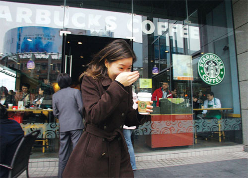 A woman holds a cup of coffee while passes by a Starbuck's Coffee shop in Shanghai. (File photo/China Daily)