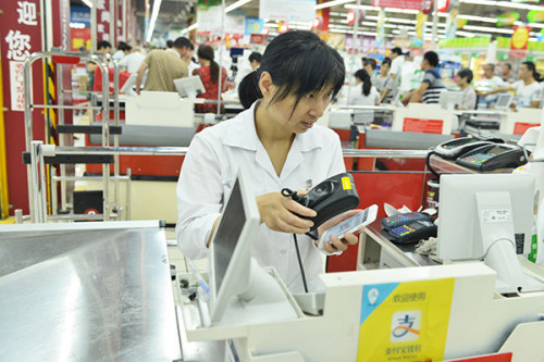 A shop assistant at a supermarket in Hangzhou, capital of Zhejiang province, scans QR code on a buyer's mobile phone. Leading Internet companies are scrambling to expand their offline operations by linking up with traditional brand name retailers. Photo/China Daily