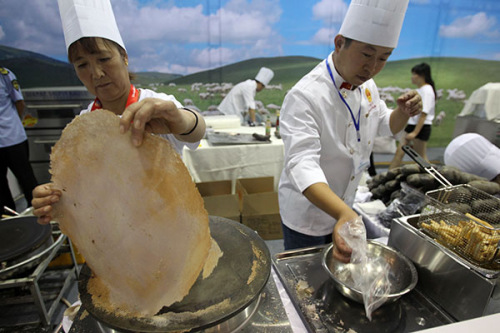 A king size pancake made of potatoes is ready to be served on a plate, while models show off giant painted potatoes at the Beijing World Potato Congress last month. (Zhang Wei/China Daily)