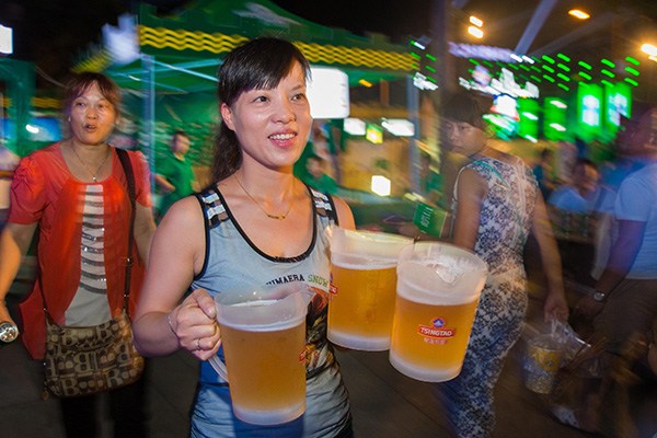 An attendant serves customers at a Tsingtao beer festival in Jiujiang, Jiangxi province. Tsingtao Brewery Co Ltd said it would buy the remaining 50 percent stake in a joint venture with Suntory Holdings Ltd for $129.5 million. (Photo/China Daily)