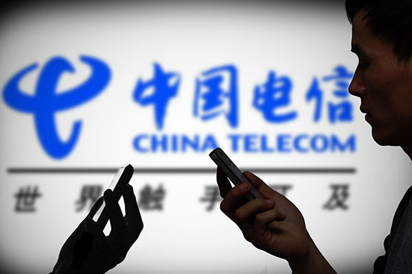 People check out their mobile phones in front of China Telecom's billboard in Beijing. (Photo provided to China Daily)