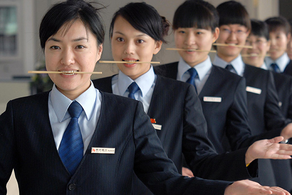 Employees of a local bank in Jinzhou, Liaoning province, practice their smiling skills with chopsticks. (Photo/China Daily)