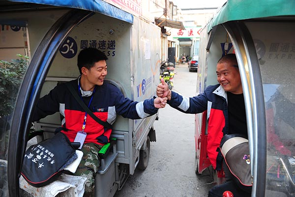 Two YTO Express couriers cheer each other up before they go to work in Fuyang, Anhui province.(Photo: China Daily/Wang Biao)