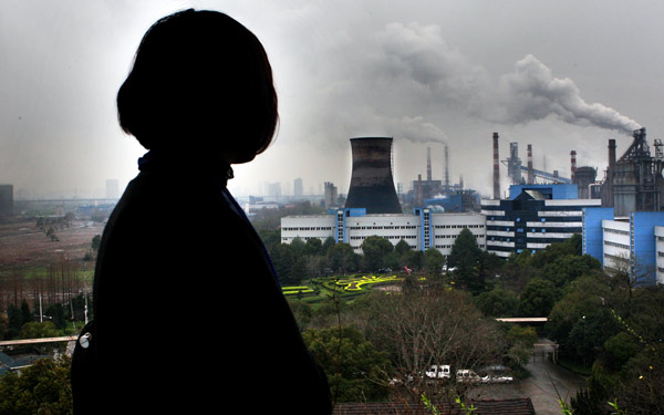 A resident looks out her home window facing the smoking chimney of a thermal power plant in Zhejiang province. Coal-fueled thermal power plants have become a major source of the country's air pollution. (Photo/China Daily)