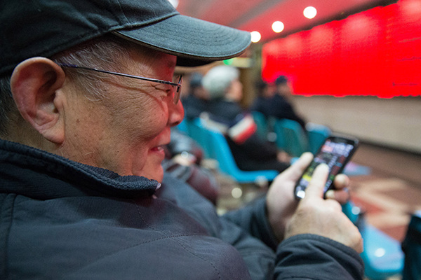 An investor browses stock information with his smartphone at a brokerage in Nanjing, Jiangsu province. (Photo provided to China Daily)