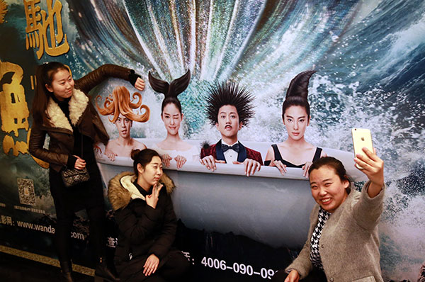 People pose in front of a poster of The Mermaid, directed by Stephen Chow, at a cinema in Beijing in February. ZOU HONG/CHINA DAILY