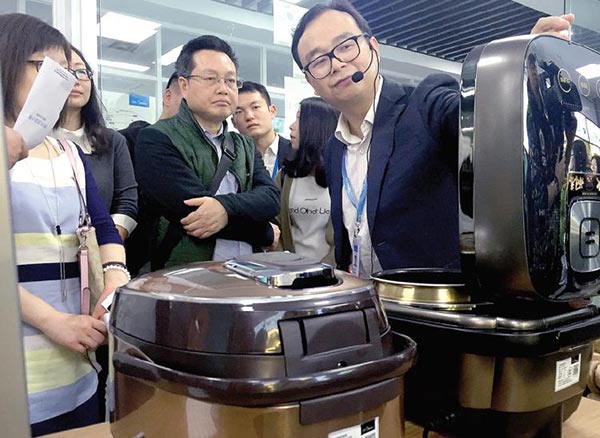 Li Guolin (right), general manager of Midea's electrical appliances division, shows consumers the latest version of the company's induction heating pressure cooker for rice. QIU QUANLIN / CHINA DAILY