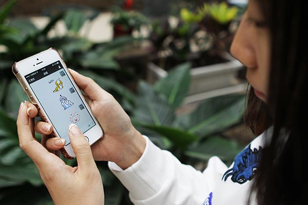 A young woman communicates with a friend with emoticons on her smartphone in Beijing. GUAN XIN / CHINA DAILY