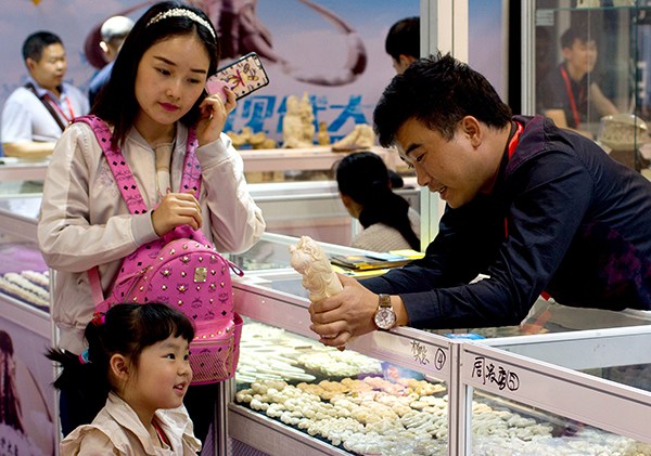 An exhibitor shows a carving to a girl at the Shanghai International Jewelry Expo 2016. The show has attracted nearly 1,000 exhibitors from 12 countries and regions. (Gao Erqiang/China Daily)