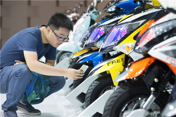 A visitor takes a photo of two-wheeled electric vehicles on display at a new energy vehicle exhibition in Nanjing, Jiangsu province.(SU YANG/CHINA DAILY)