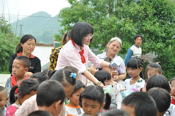 Liu Jiaying (wearing glasses) distributes gifts to students at Shaba primary school in Qianxi county, Guizhou province while visiting the school for the launch ceremony of the first Flying Box project in June, 2015. (Provided to CHINA DAILY)