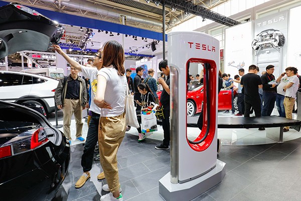 Tesla post stands beside a Tesla model during a recent auto fair in Beijing. (Photo/China Daily)