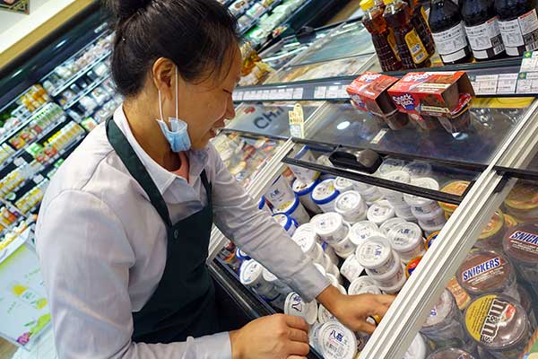 A worker puts boxes of ice cream in a refrigerator at a BHG supermarket in Beijing.(Photo by Wang Zhuangfei/China Daily)