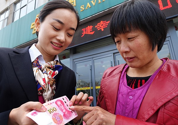 An employee shows a customer anti-counterfeiting marks on a new banknote at Postal Savings Bank of China's branch in Zaozhuang, Shandong province. (Photo/China Daily)
