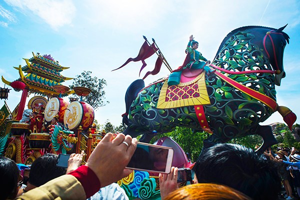 Visitors take pictures using mobile phones while a performer dressed as a Chinese traditional nomadic hero joins a parade of floats at Shanghai Disney Resort. (Photo provided to China Daily)