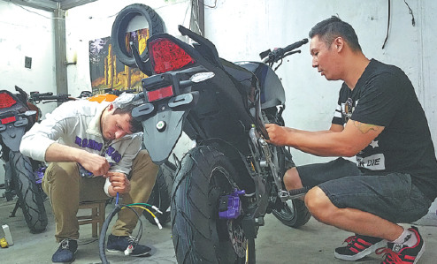 Nathan Siy (right), a Canadian-born passionate motorcycle rider and CEO of Evoke Motorcycles, works together with his employee to fix a motorcycle. (Photo provided to China Daily)