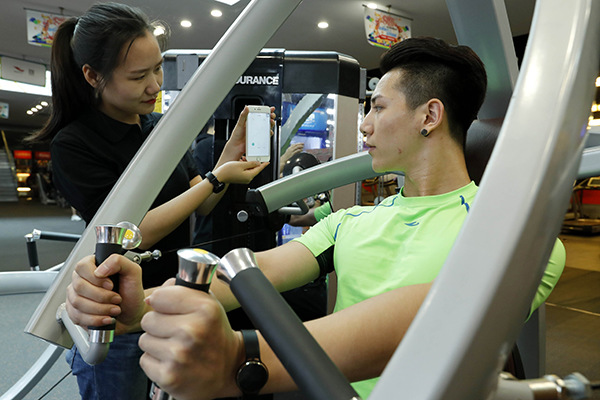 A fitness program consumer checks readings on an app while exercising at a club in Beijing. (Photo/Xinhua)