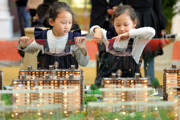 Twin sisters check out a model of a building at a real estate expo in Nanjing. The second-child policy is expected to fuel people's demand for larger homes. (Photo by You You/For China Daily)
