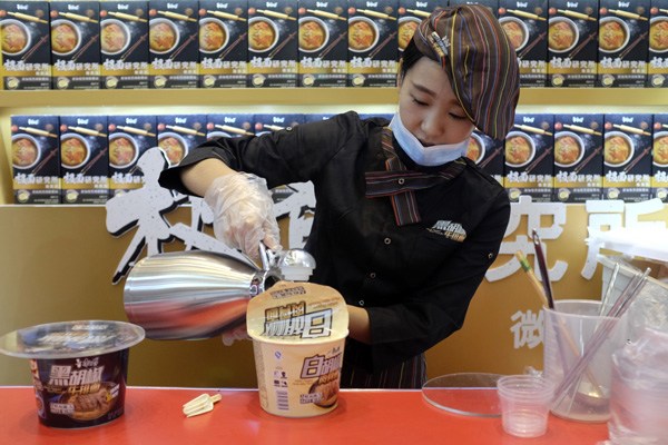 A salesperson prepares a bowl of instant noodles at a food fair in Beijing in September. (Photo by Dafei/For China Daily)