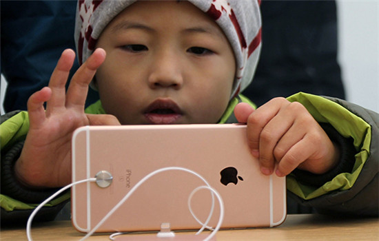 A boy plays with a smartphone in an outlet of Apple Inc in Qingdao, Shandong province. (Photo/China Daily)