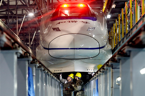Two technicians inspect a high-speed train's wheels at a maintenance shed in Nanjing, Jiangsu province. [Photo provided to China Daily]
