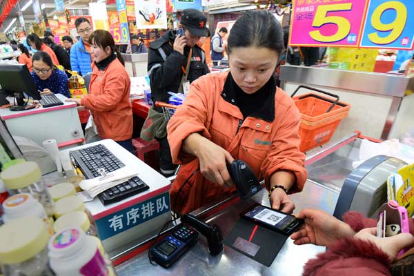 A supermarket employee in Wuhan, capital of Hubei province, scans a consumer's mobile phone to finish payment during last year's Double 12 shopping festival. (hoto by Jin Siliu/For China Daily)