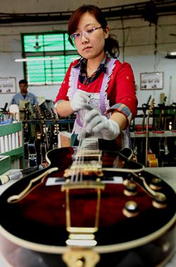 A technician fixes strings to a guitar at a musical instrument factory in Zaozhuang, Shandong province. (Photo/China Daily)