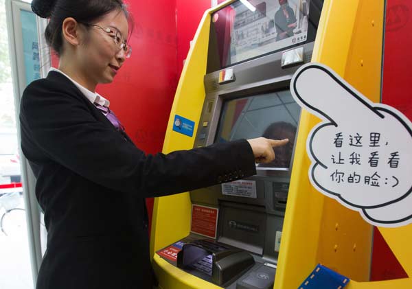 A bank clerk demonstrates cash withdrawal from an ATM that uses the facial recognition technology, in Nanjing, Jiangsu province. (Photo by Su Yang/For China Daily)