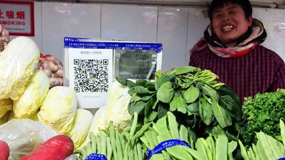 A vendor in a vegetable market shows the QR code for WeChat Pay. (Photo/CGTN) 
