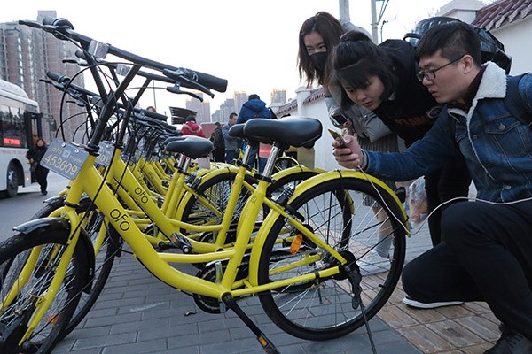 Riders scan ofo bikes in Xi'an, Shaanxi province. The bike-hire startup is experimenting with a deposit waiver system for users in Shanghai and may extend the service to other cities in the country. (Photo/China Daily)