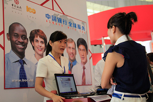 A clerk (left) in an outlet of Bank of China in Haikou, Hainan province, answers a customer's queries. (Photo/China Daily)