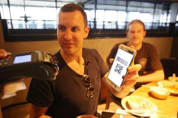 Tim Clancy, from Australia, pays a bill with his smartphone at a restaurant in Hangzhou, Zhejiang province, on Friday. (Photo provided to China Daily)