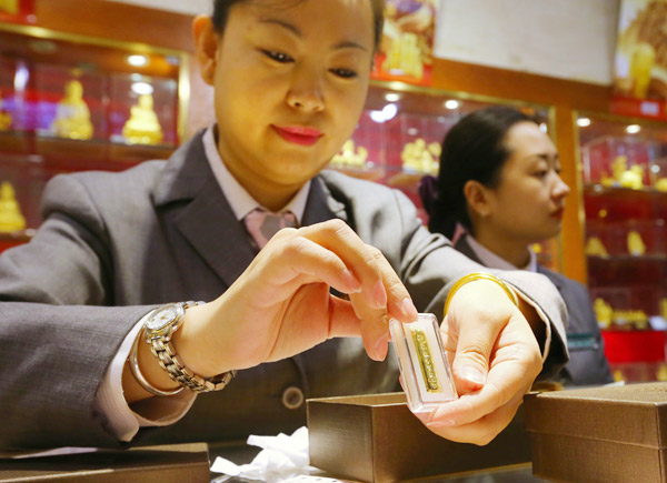 A worker displays a gold bar at a department store in Beijing. JIANG DONG / FOR CHINA DAILY
