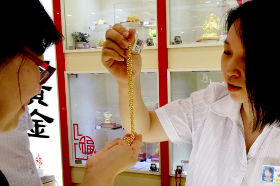 A shop assistant helps a customer to choose gold jewelry in Beijing. (Photo: CAO BOYUAN / FOR CHINA DAILY)