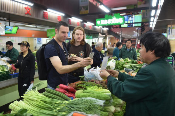 Foreigners experience using mobile payments to buy vegetables at a marketplace in Hangzhou, Zhejiang province, on April 14, 2017. (Photo/Xinhua