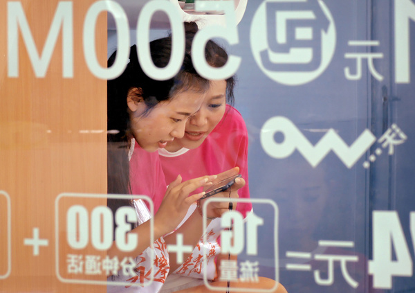 Two women surf the web on a mobile phone at an outlet of China Unicom in Nanjing, capital of Jiangsu province. AN XIN / FOR CHINA DAILY