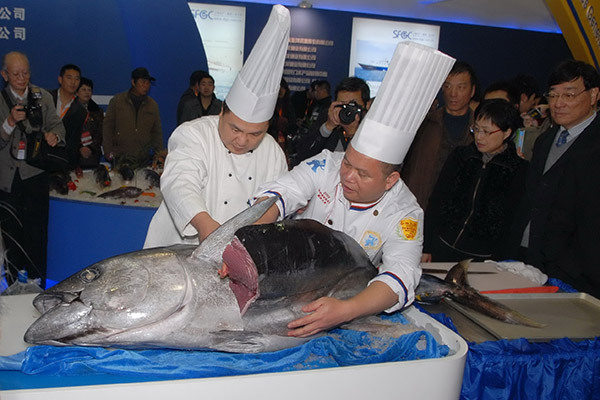 Two employees from Shanghai Fisheries Group Co Ltd serve tuna at an industry expo held in Shanghai. (Photo/China Daily)