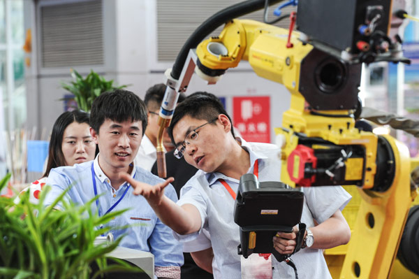 A technician introduces how a robotic arm works at a machinery expo in Harbin, capital of Heilongjiang province. (Photo/Xinhua)