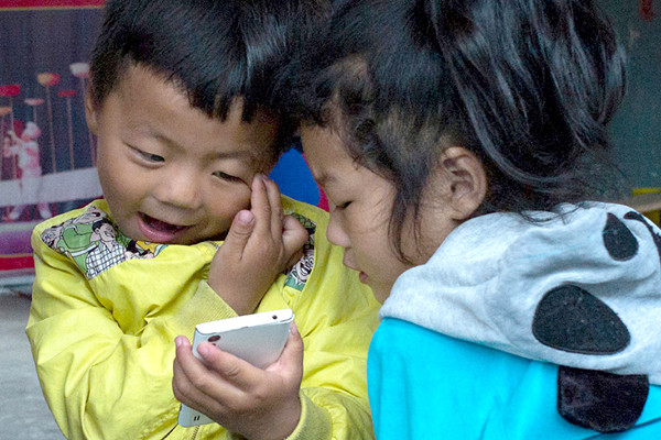Two kids in Yangshang county, Anhui province, play games on a mobile phone. (Photo/Xinhua)