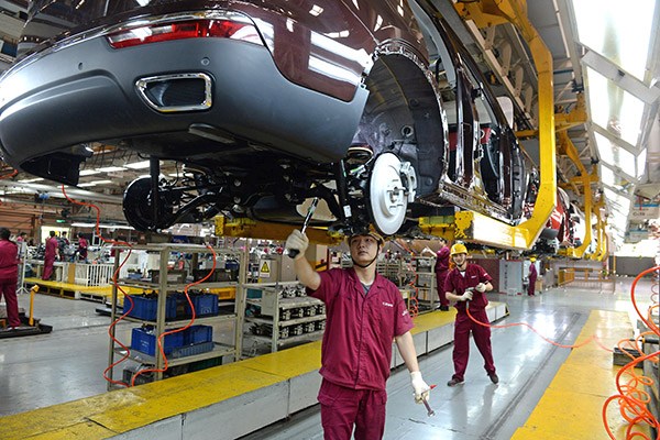 Workers install chassis on a production line of JAC Motors. (Photo/China Daily)