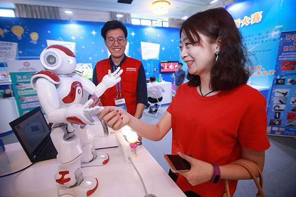 A visitor shakes hands with a robot during a science and technology week in Beijing. (Photo/China Daily)