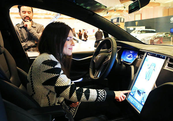 A woman experiences the touch screen of a Tesla car during an auto expo in Toronto, Canada. (Photo/Xinhua)