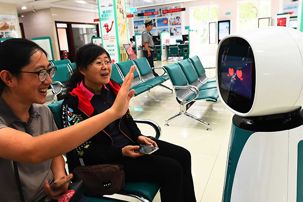Two women interact with a robot, which helps handle business, at an outlet of Agricultural Bank of China in Qingzhou, Shandong province. (Photo/China Daily)