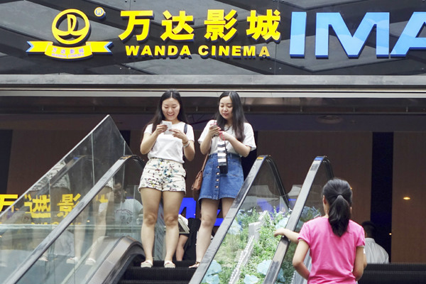 Two moviegoers check their mobile phones at a Wanda cinema in Zhengzhou, capital of Henan province. (Photo provided to CHINA DAILY)