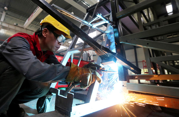 A worker welds parts for a new energy car in a manufacturing workshop. (Photo by Tan Kaixing/For China Daily)