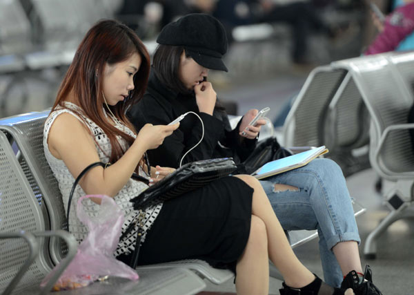 Passengers at Jiangxi railway station read e-novels on their mobile phones while waiting for their train to arrive. (Photo by Hu Guolin/For China Daily)