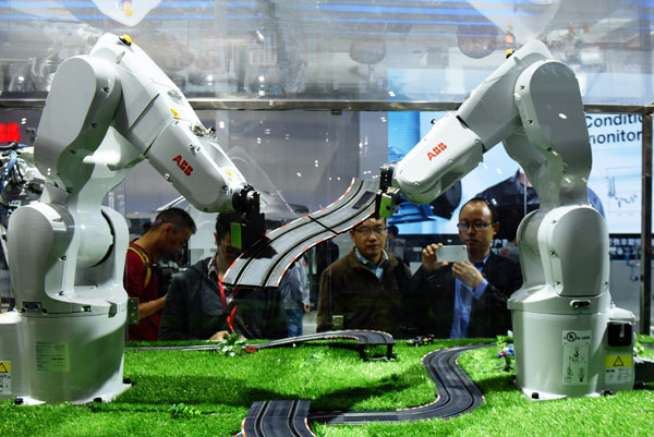 Visitors watch ABB robots build a model at an exhibition in Shanghai. (Photo by Long Wei/For China Daily)